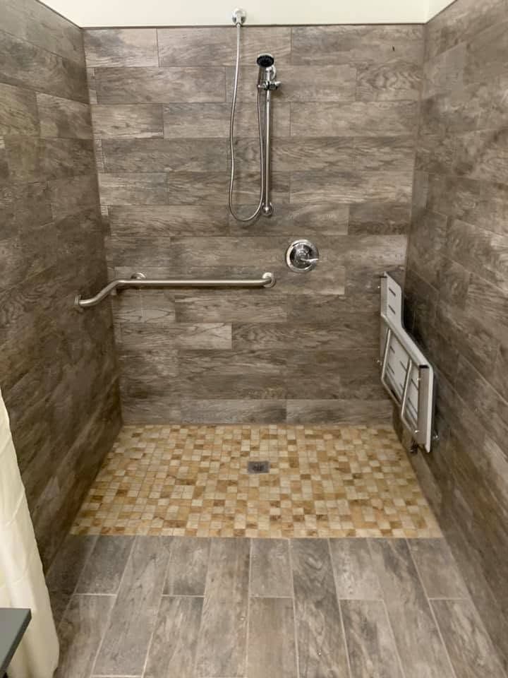 Tiled roll-in shower with a handheld shower head on a slide bar, grab bar and fold-down seat