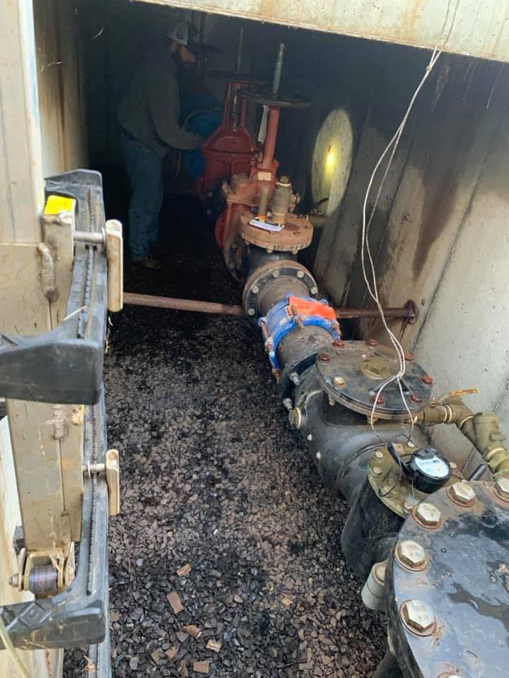 Plumber working in an underground vault beside large water service piping and gate valves